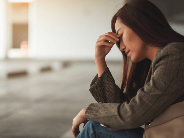 Mid-age woman sitting in a parking garage with her head down portraying the need to consider paying for drug and alcohol addiction treatment